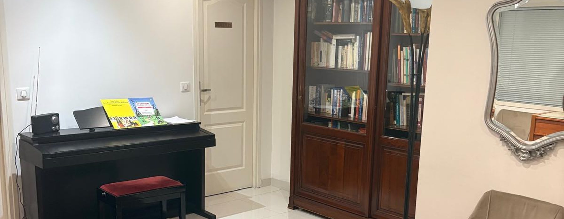 La salle d'attente du cabinet : un piano, une bibliothèque ancienne et un fauteuil.